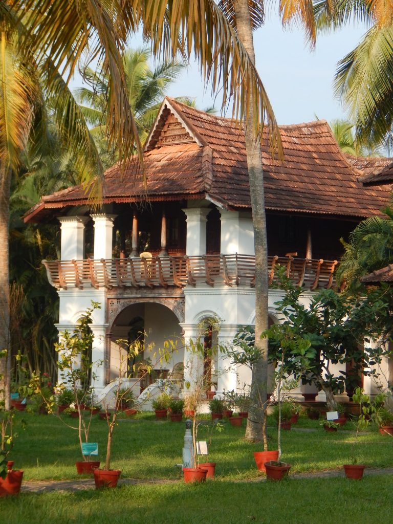 Traditional South Indian heritage villa with a green lawn and coconut palms